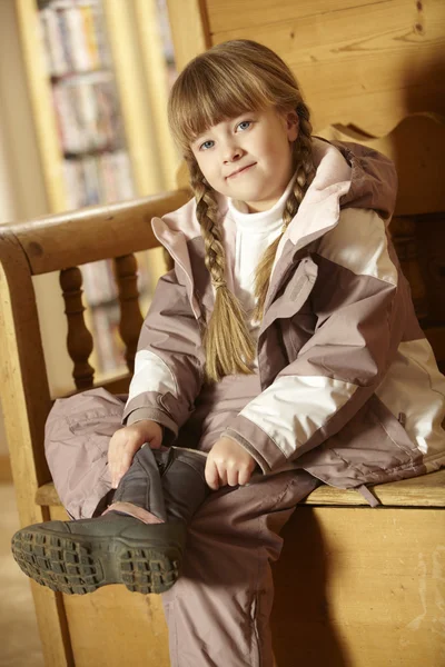 Молодая девушка, сидящая на деревянном сиденье, одетая в теплую открытую одежду — стоковое фото