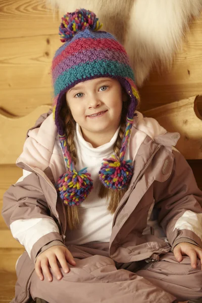 Junges Mädchen sitzt auf Holzsitz und trägt warme Outdoor-Kleidung — Stockfoto