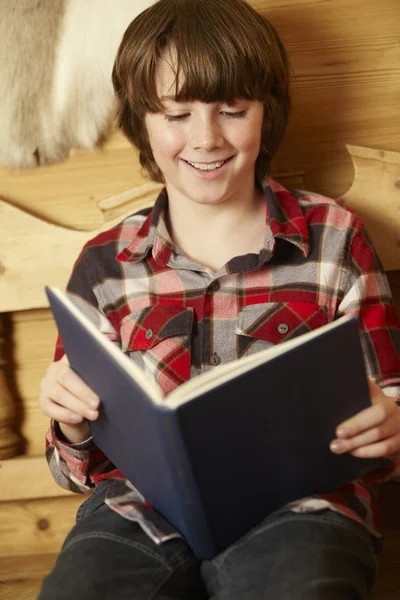 Junge sitzt auf Holzsitz und liest Buch — Stockfoto