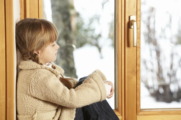 Karlı manzaraya bakarak pencere çıkıntının üzerinde oturan genç kız — Stok fotoğraf