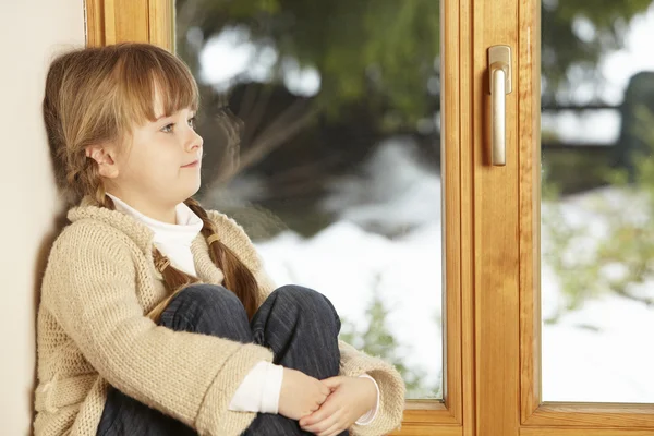 Karlı manzaraya bakarak pencere çıkıntının üzerinde oturan genç kız — Stok fotoğraf