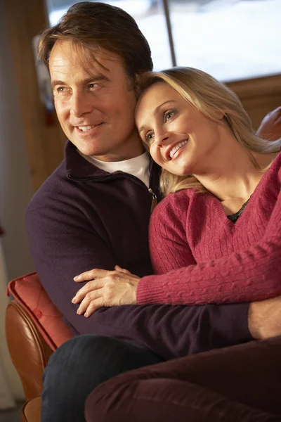 Paar mittleren Alters plaudert auf Sofa im Chalet mit Winterblick — Stockfoto