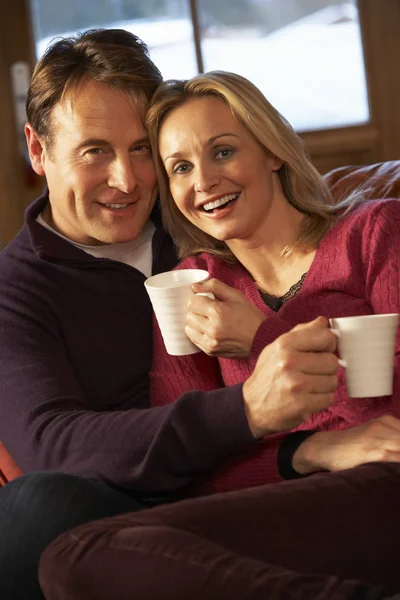 Casal de meia idade sentado no sofá com bebidas quentes — Fotografia de Stock