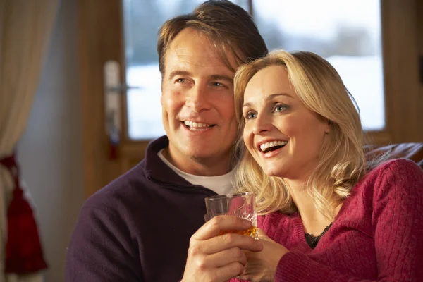 Middle Aged Couple Sitting On Sofa With Glasses Of Whisky Watchi — Stock Photo, Image