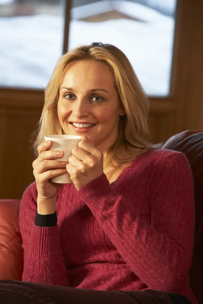 Donna di mezza età che si rilassa con bevanda calda sul divano guardando la TV — Foto Stock