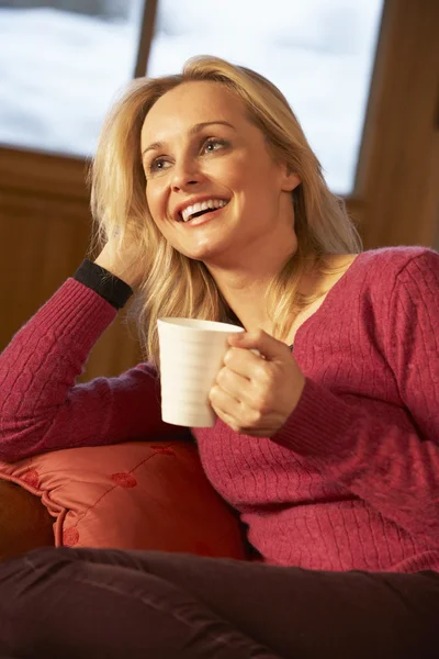 Mulher de meia-idade relaxante com bebida quente no sofá assistindo TV — Fotografia de Stock