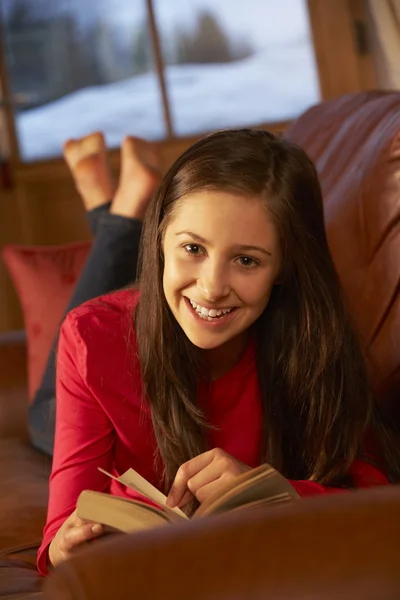 Девочка-подросток отдыхает на диване читая книгу — стоковое фото