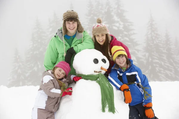 Группа детей, строящих снеговика на лыжном отдыхе в горах — стоковое фото