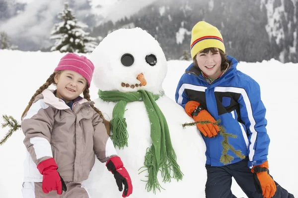 Twee jonge kinderen gebouw sneeuwpop op skivakantie in Bergen — Stockfoto