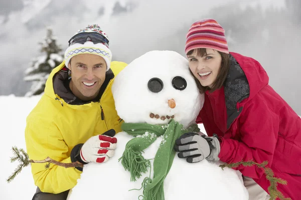 Ehepaar mittleren Alters baut Schneemann im Skiurlaub in den Bergen — Stockfoto