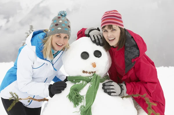 Två kvinnliga vänner bygga snögubbe på skidsemester i bergen — Stockfoto