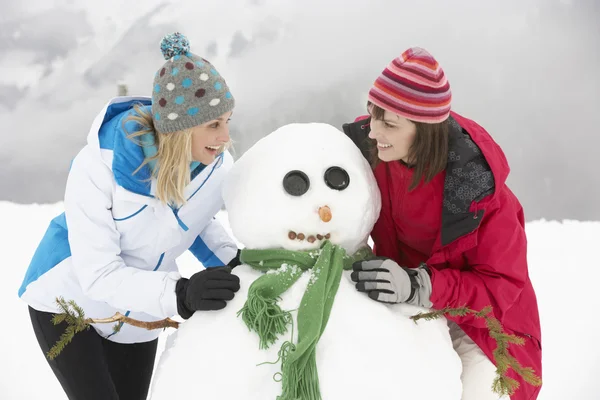 Duas amigas do sexo feminino construindo boneco de neve em férias de esqui em montanhas — Fotografia de Stock
