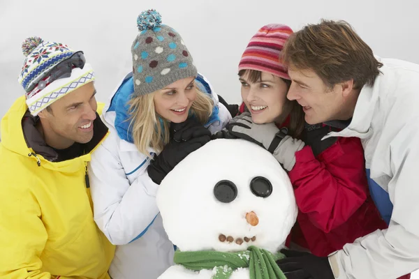 Skupina přátel, staví sněhuláka na lyžařské dovolené v horách — Stock fotografie