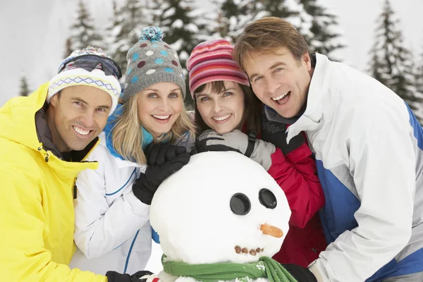 Skupina přátel, staví sněhuláka na lyžařské dovolené v horách — Stock fotografie
