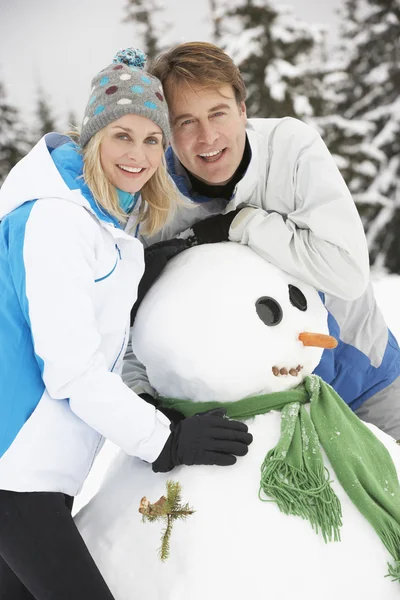 Mellersta åldern par bygga snögubbe på skidsemester i bergen — Stockfoto