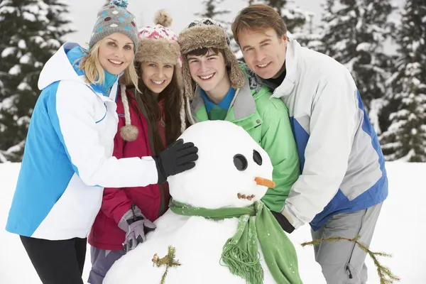 Adolescente familia edificio muñeco de nieve en vacaciones de esquí en las montañas —  Fotos de Stock