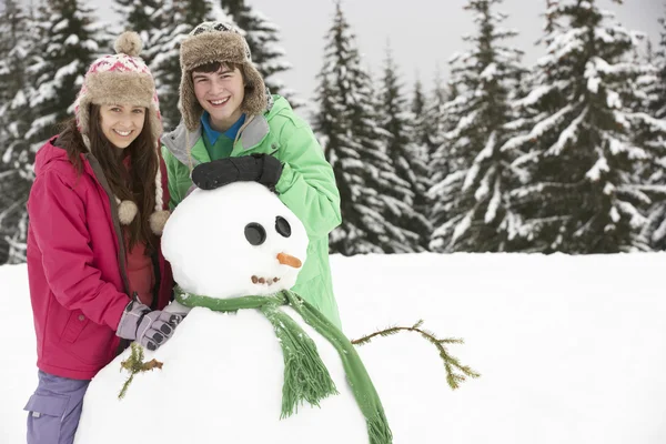 Dva teenageři staví sněhuláka na lyžařské dovolené v horách — Stock fotografie