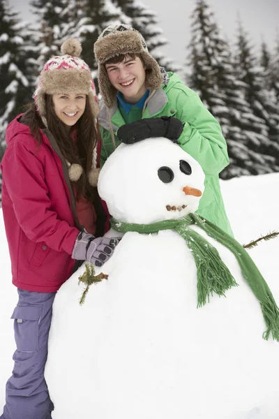 Dois adolescentes construindo boneco de neve em férias de esqui em montanhas — Fotografia de Stock