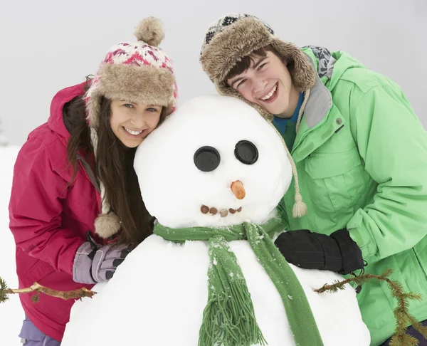 Dva teenageři staví sněhuláka na lyžařské dovolené v horách — Stock fotografie
