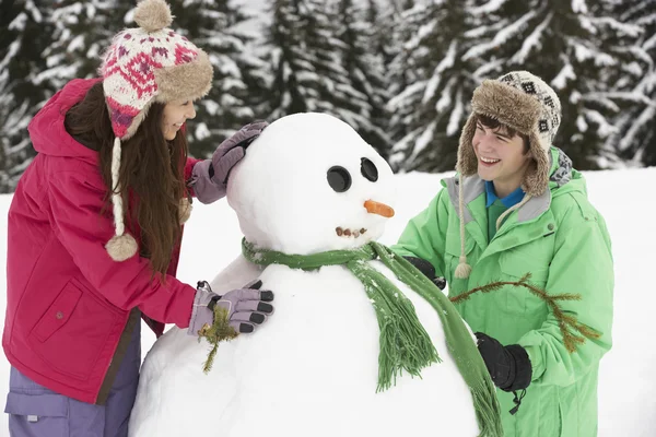 Dois adolescentes construindo boneco de neve em férias de esqui em montanhas — Fotografia de Stock