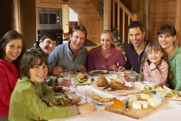 Två familes njuter måltid i alpin chalet tillsammans — Stockfoto