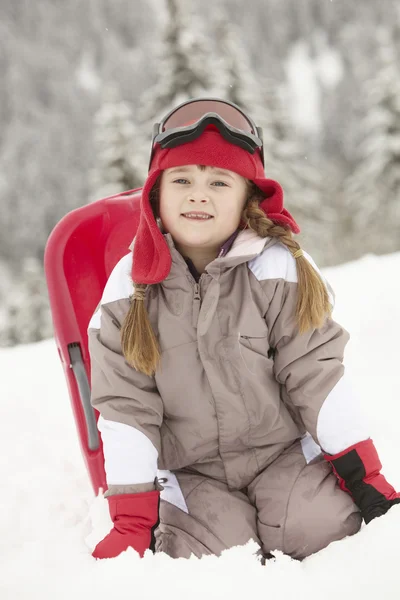 Junges Mädchen spielt im Skiurlaub im Gebirge mit Schlitten im Schnee — Stockfoto