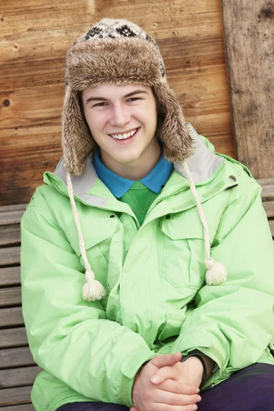 Nastoletni chłopiec ubrany na zimnie, siedząc na ławeczce, drewniane — Zdjęcie stockowe