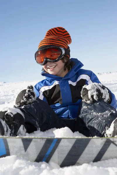 年轻的男孩坐在雪与单板滑雪 — 图库照片