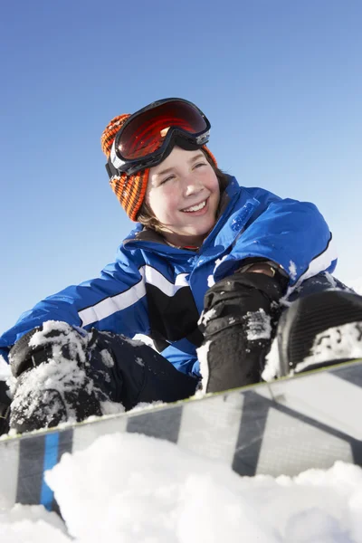 年轻的男孩坐在雪与单板滑雪 — 图库照片