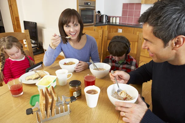 Familia comiendo el desayuno juntos en la cocina mientras los niños juegan —  Fotos de Stock