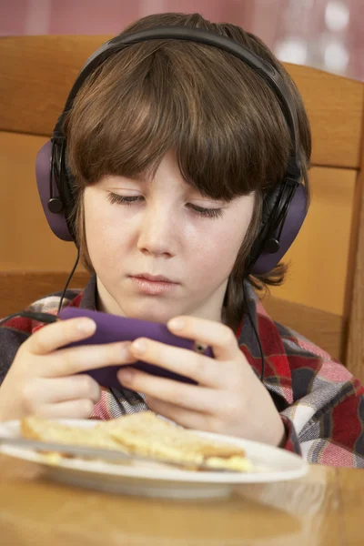Chlapec hraje s ručně držené herní konzole, zatímco jíst snídani — Stock fotografie