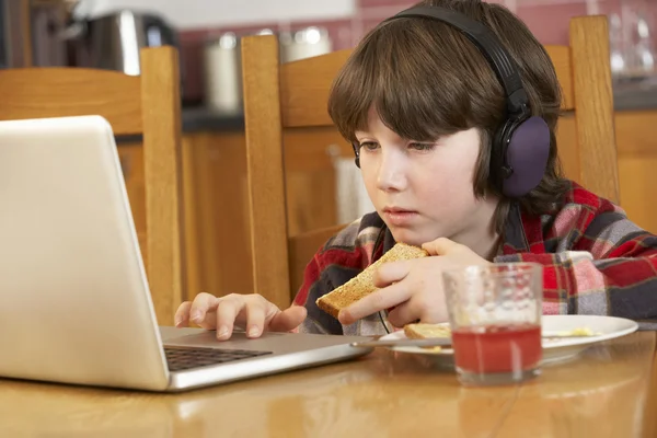 Niño usando el ordenador portátil mientras come el desayuno — Foto de Stock