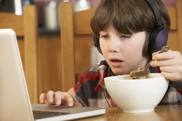 Niño usando el ordenador portátil mientras come el desayuno — Foto de Stock