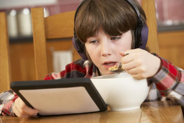 Chłopiec przy użyciu komputera typu tablet, podczas gdy jedzenie śniadanie — Zdjęcie stockowe