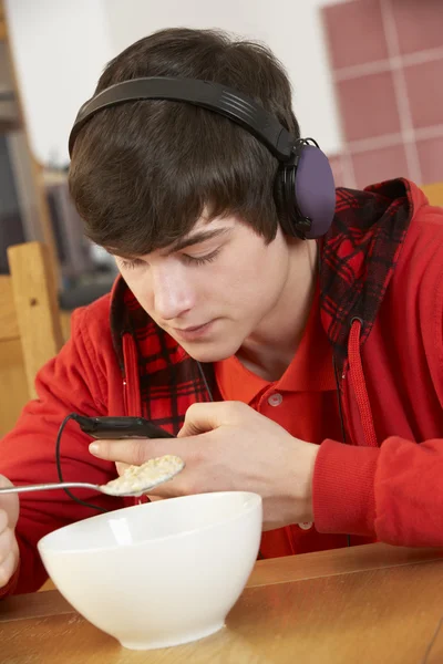 Adolescente menino ouvindo MP3 Player enquanto come café da manhã — Fotografia de Stock