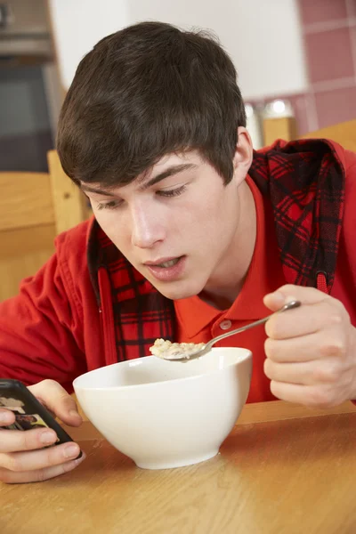 Adolescente menino adolescente mensagens de texto enquanto come café da manhã — Fotografia de Stock