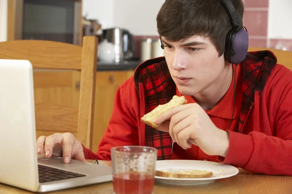 十几岁的男孩使用膝上型电脑，虽然吃早餐 — 图库照片
