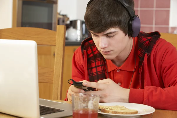 Teenage Boy Using Laptop And Listening to MP3 Player Whilst Eati — стоковое фото