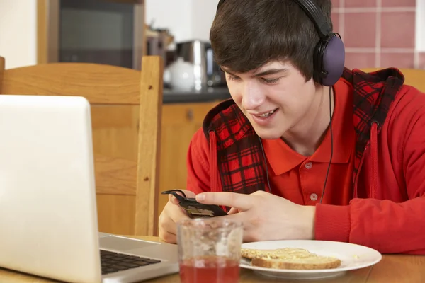 Tiener met behulp van laptop en luisteren naar mp3-speler terwijl eati — Stockfoto