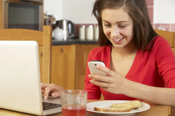 十几岁的女孩在吃饭的时候 breakfa 使用笔记本电脑和移动电话 — 图库照片