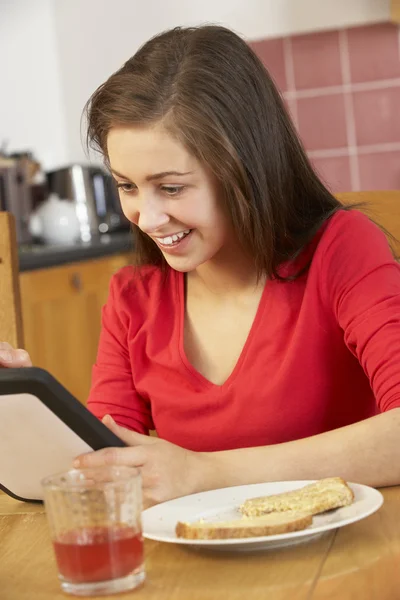朝食を食べながらタブレット コンピューターを使用して十代の少女 — ストック写真