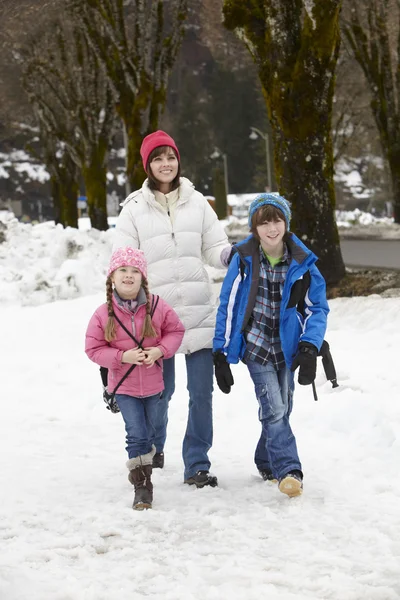 Mãe andando duas crianças para a escola ao longo da rua nevado no esqui — Fotografia de Stock