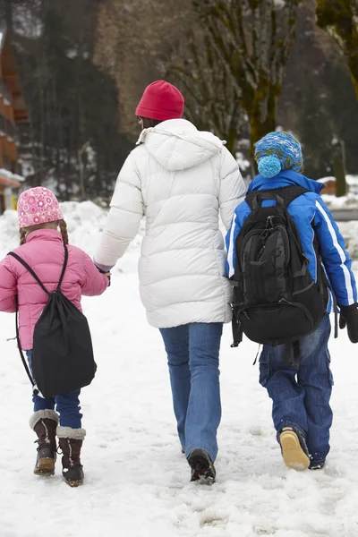 Madre walking due bambini a scuola lungo neve strada in sci — Foto Stock