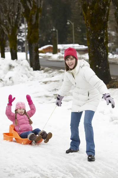 母亲把女儿拉雪橇滑雪决议在雪街沿上 — 图库照片