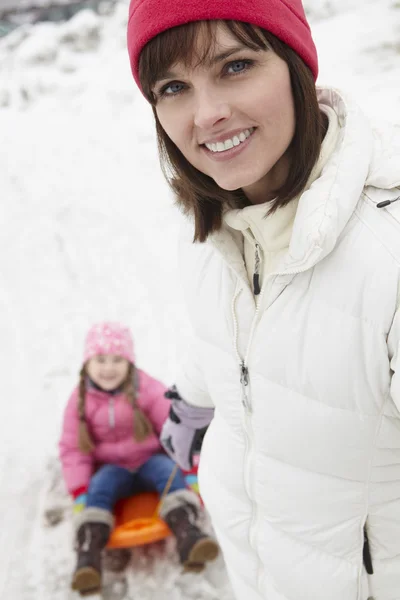 Mère tirant sa fille sur luge le long de la rue enneigée dans la station de ski — Photo