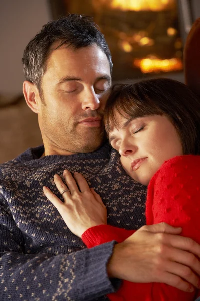 Middle Aged Couple Cuddling On Sofa By Cosy Log Fire Stock Image