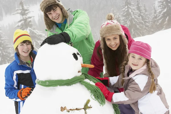Grupo de niños construyendo muñeco de nieve en vacaciones de esquí en las montañas Imagen de archivo