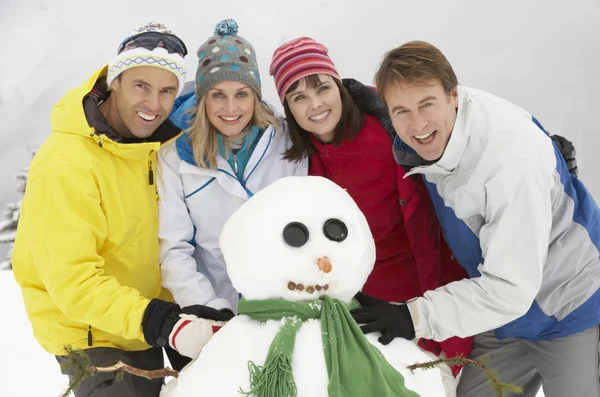 Grupo de amigos construyendo muñeco de nieve en vacaciones de esquí en las montañas Imágenes de stock libres de derechos