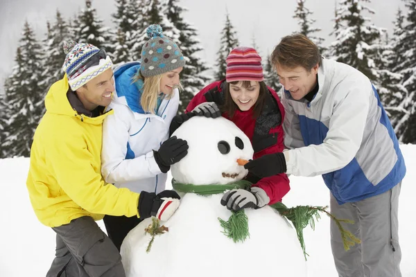 Grupo de amigos construyendo muñeco de nieve en vacaciones de esquí en las montañas Imagen de archivo