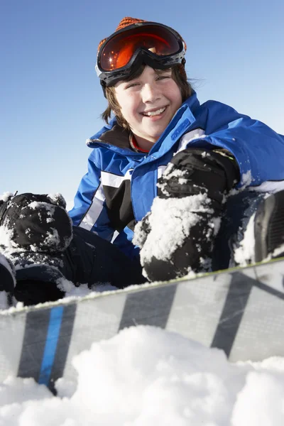 Junge sitzt mit Snowboard im Schnee Stockbild